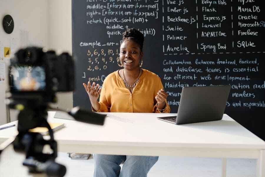 African American teacher sitting at table in front of camera and recording her blog about IT