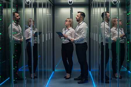 Man and women in data center looking a rack of servers