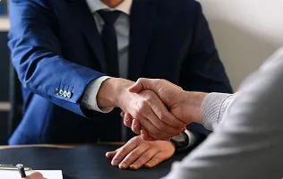 Two business people in suits shaking hands over a desk