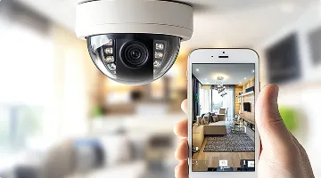 A person's hand holding a smartphone displaying a live view of the living room, representing an Integrated Security System