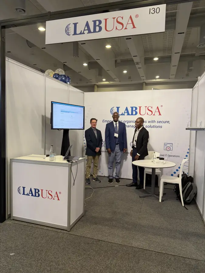 Three LABUSA representatives standing at booth 130 during a trade show; with branded banner and monitor display.