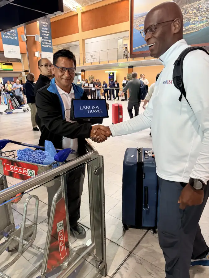 LT representative shakes hands with LABUSA Travel rep holding a tablet at Cape Town International Airport arrivals hall.