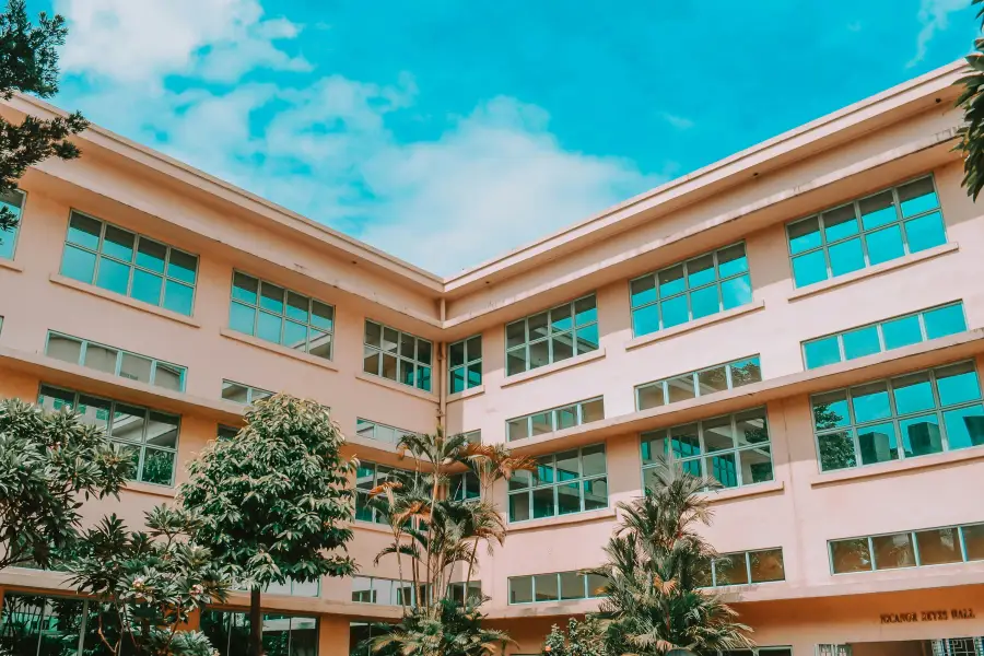 Exterior view of Reyes Hall; a multi-story institutional building with large windows and tropical landscaping under a blue...