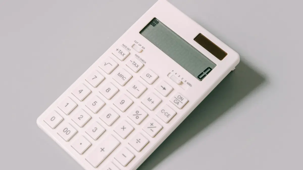 A plain white desk calculator lying on a light grey surface.