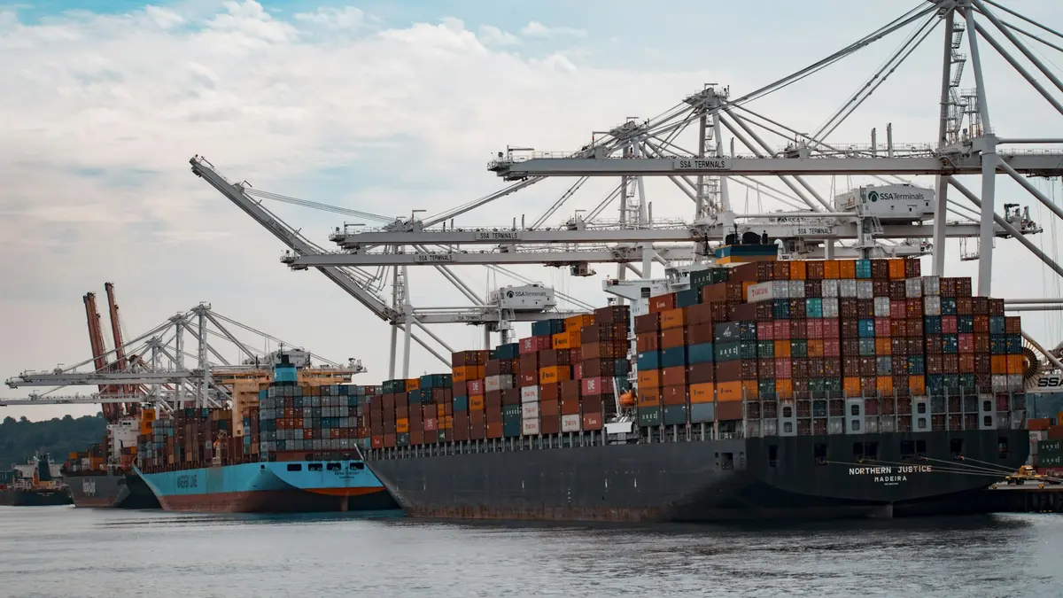 A container ship stacked with freight containers alongside gantry cranes at a port.