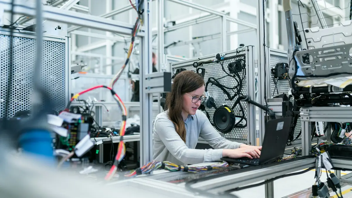 An engineer at a laptop beside an automated production line, monitoring the machinery.
