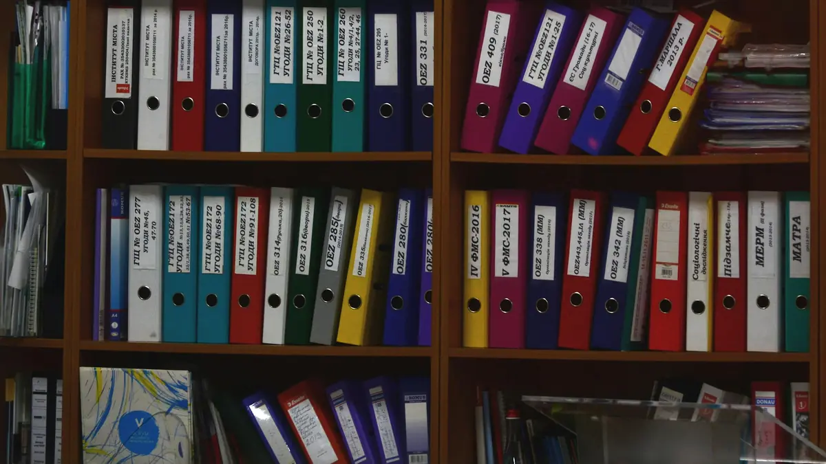 Wooden shelves holding rows of coloured ring binders, each with a written spine label.