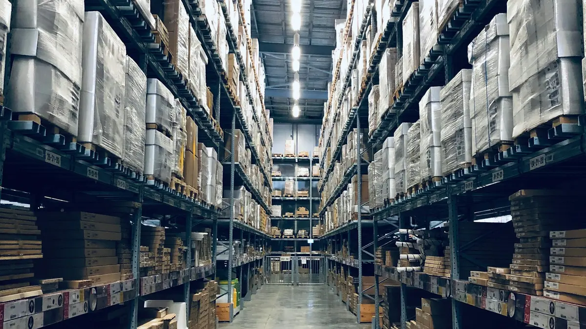 A long aisle between tall warehouse racks stacked with boxed and palletised stock.