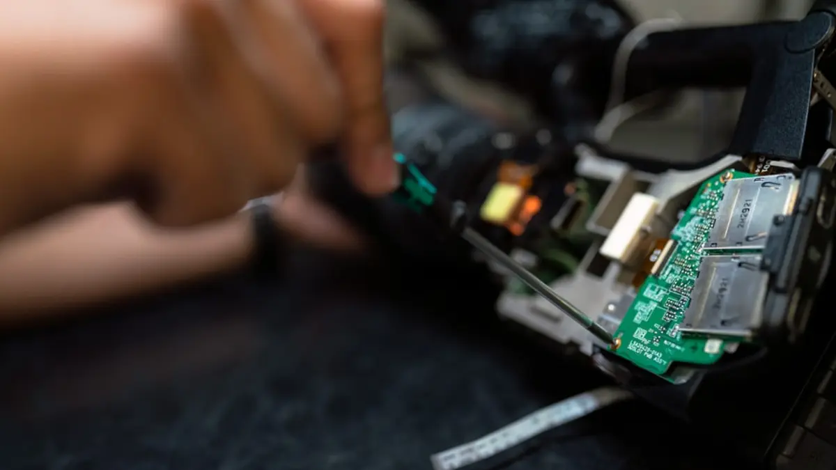 Hands using a small precision tool to examine the exposed circuit boards inside a device.