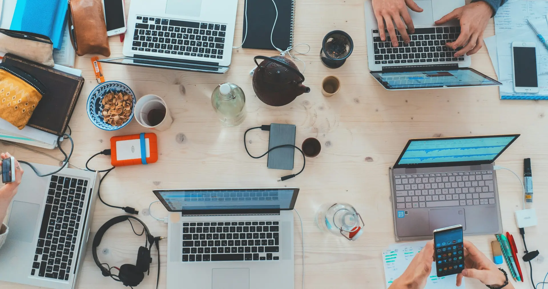 Overhead view of a team working across laptops, tablets and a phone on one shared desk.
