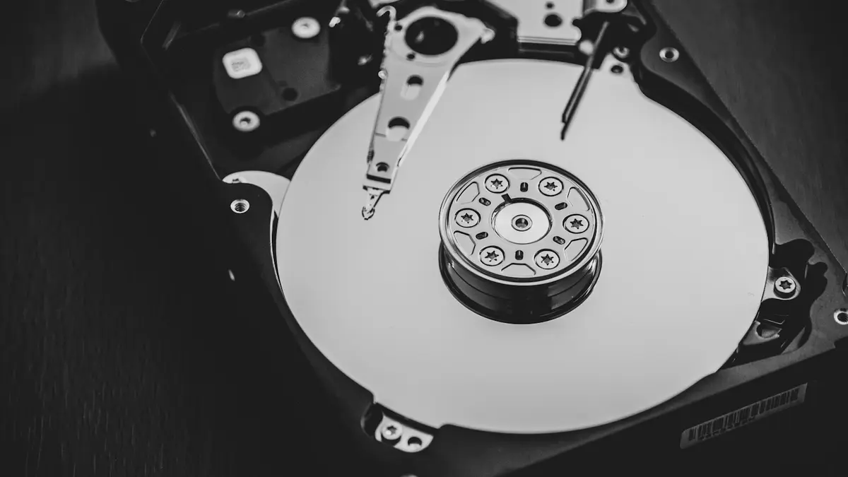 An opened hard disk drive in black and white, showing the platter and the read head arm.