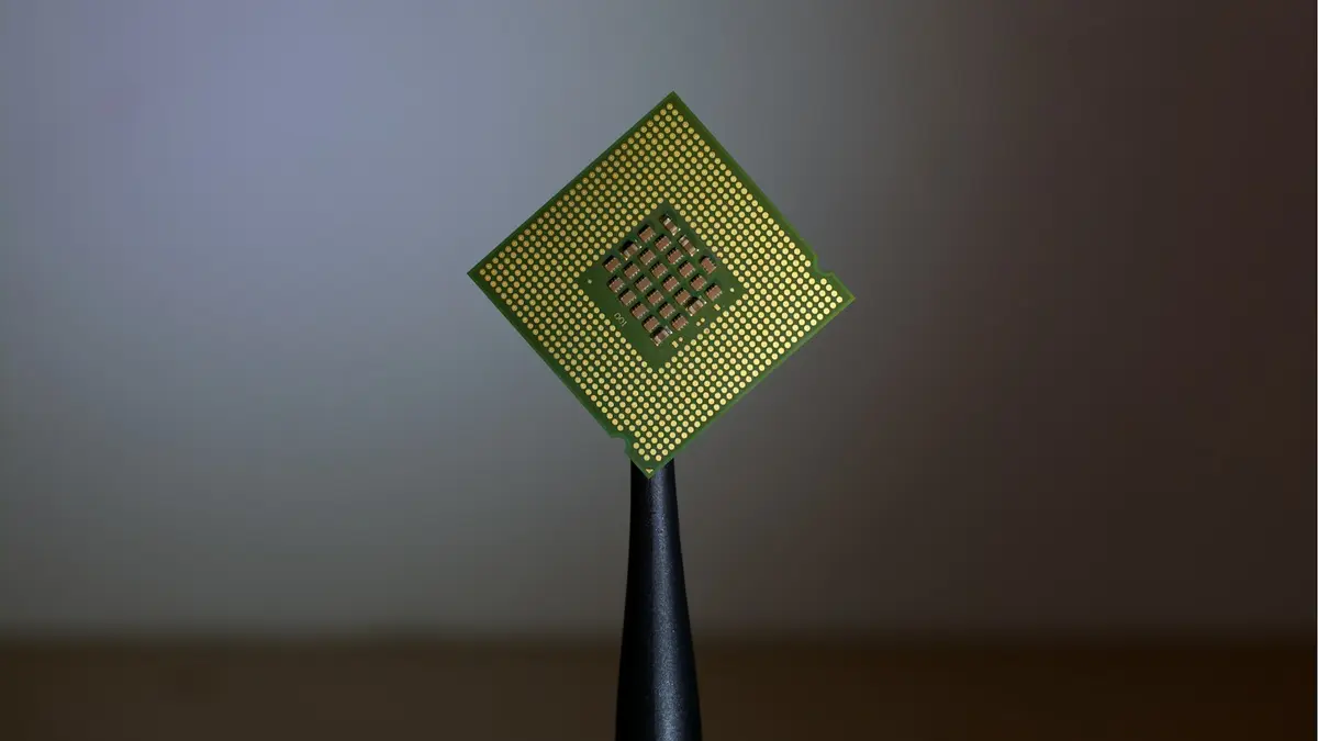 A small gold and green processor die balanced on a black stand against a plain background.
