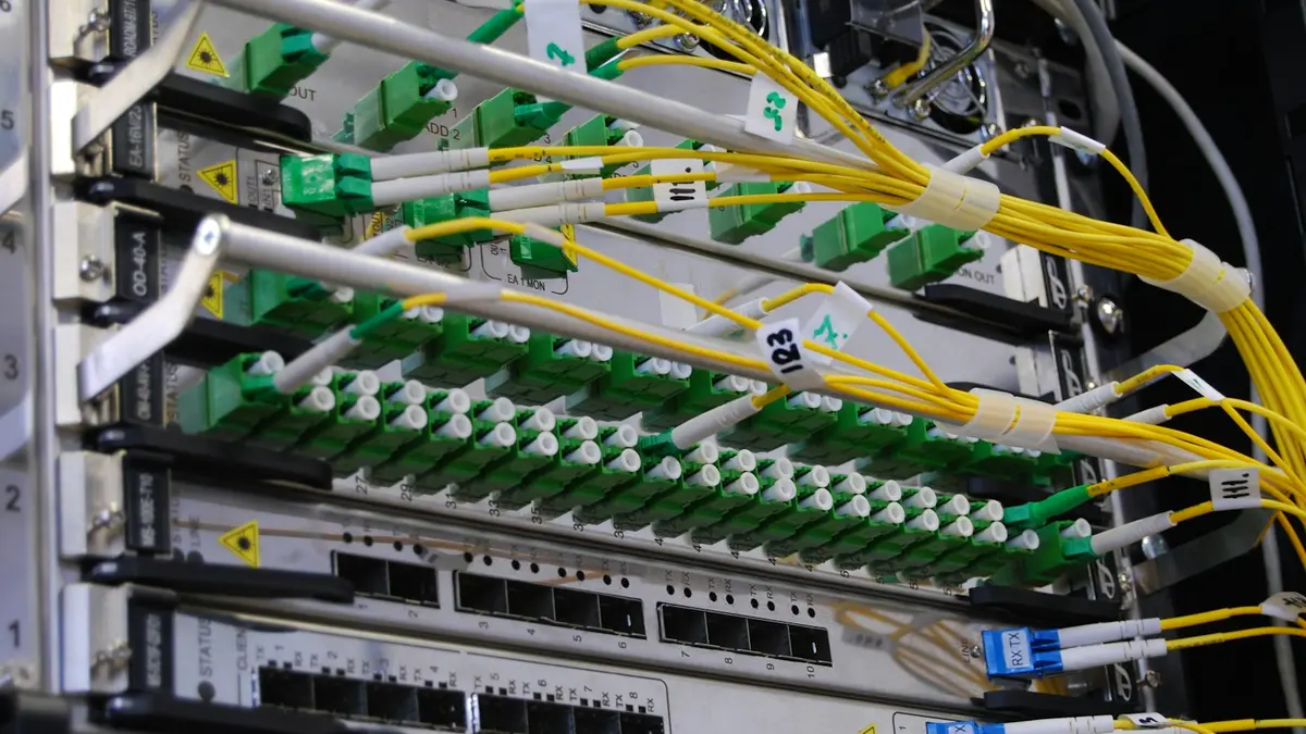 A fiber optic patch panel with green and yellow cables routed in dense ordered rows.