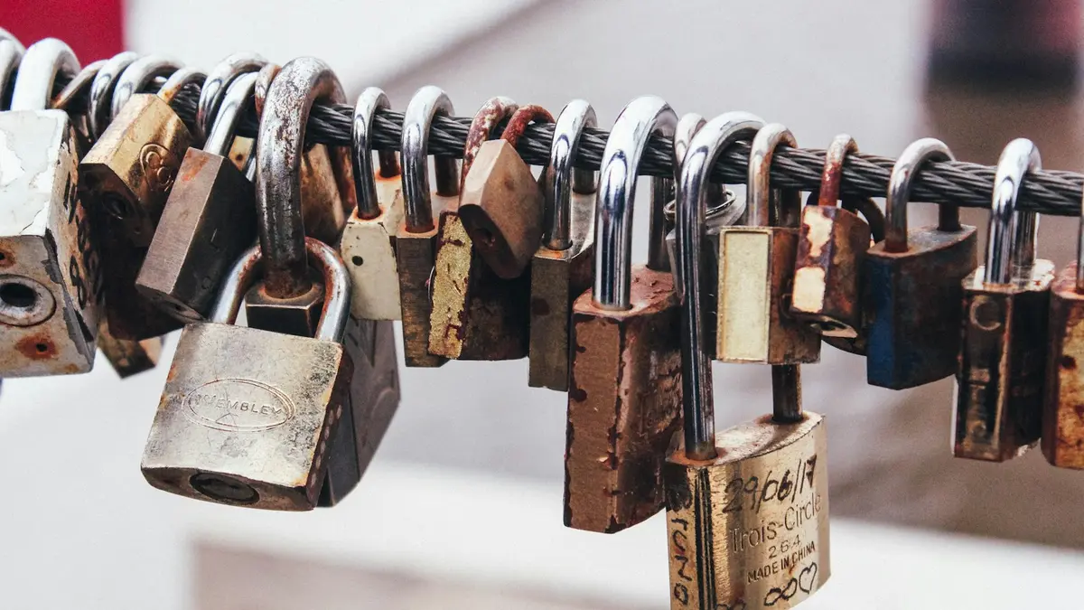 A row of weathered brass and steel padlocks fastened side by side along a metal rail.