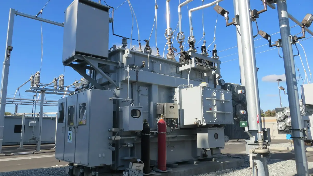 Transformer and switchgear equipment in an electrical substation under a clear blue sky.