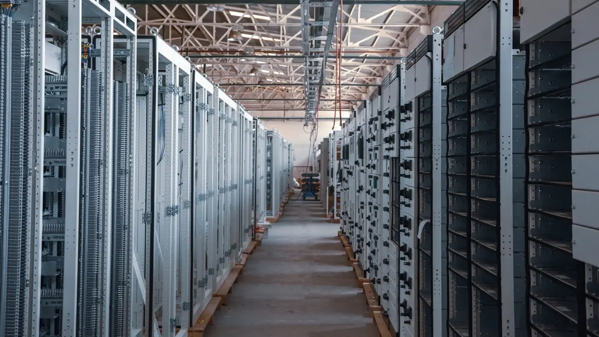 A walkway running between tall grey storage racks in a brightly lit data center hall.