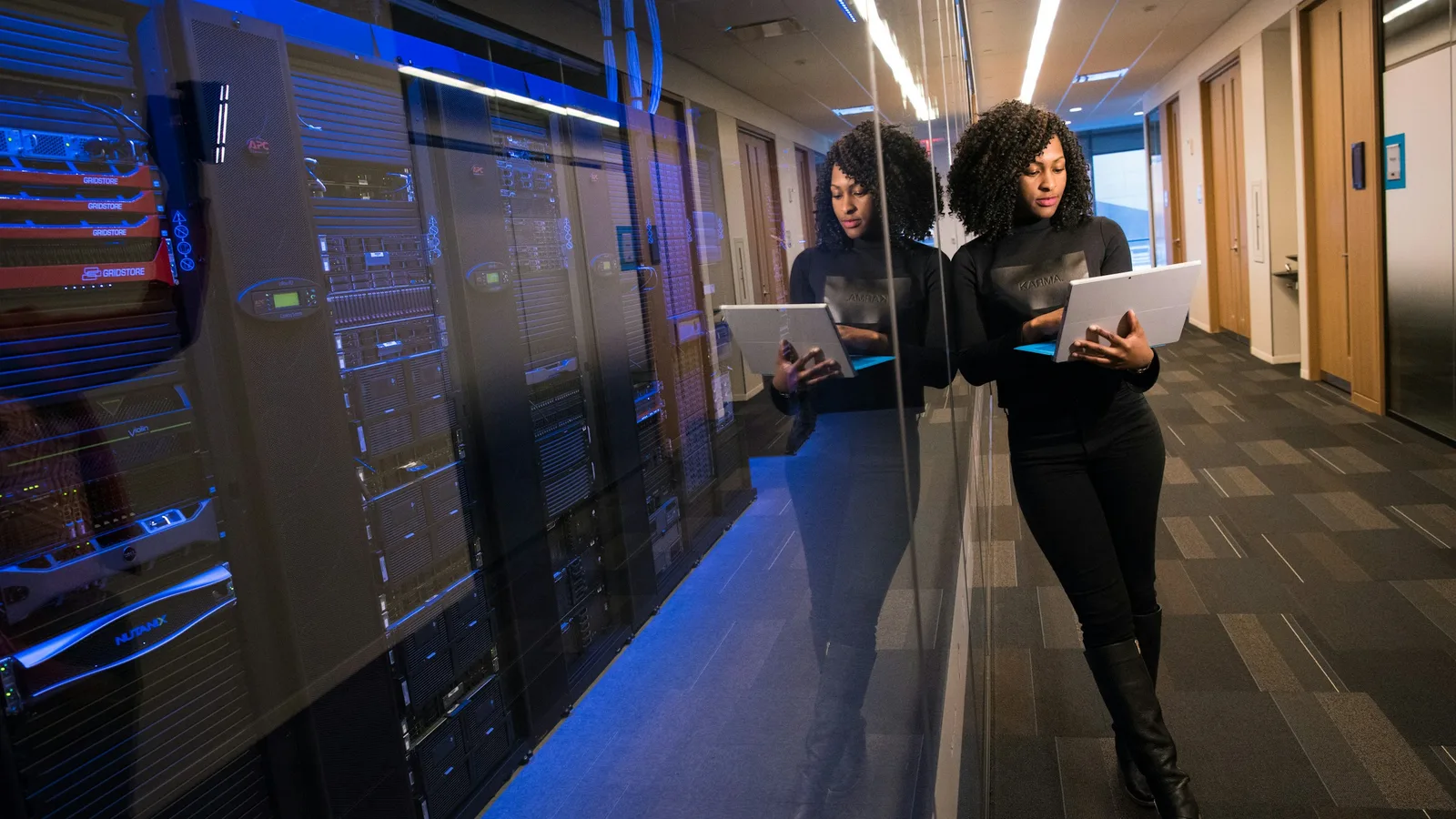 A technology professional holding a laptop beside racks of data center equipment.