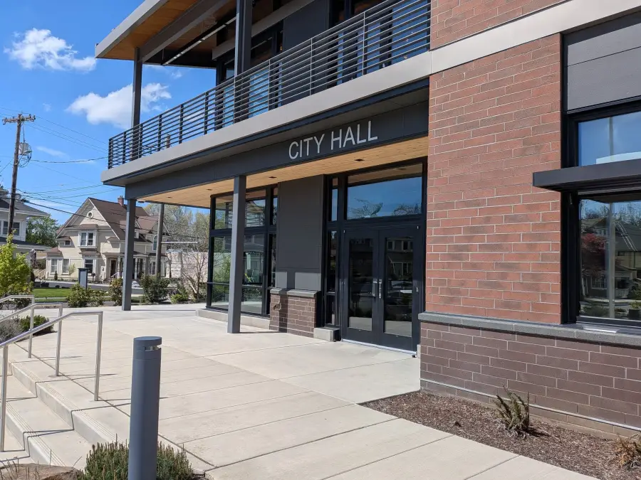 Modern city hall entrance with a brick facade, glass doors, an accessible ramp and a second-floor balcony.