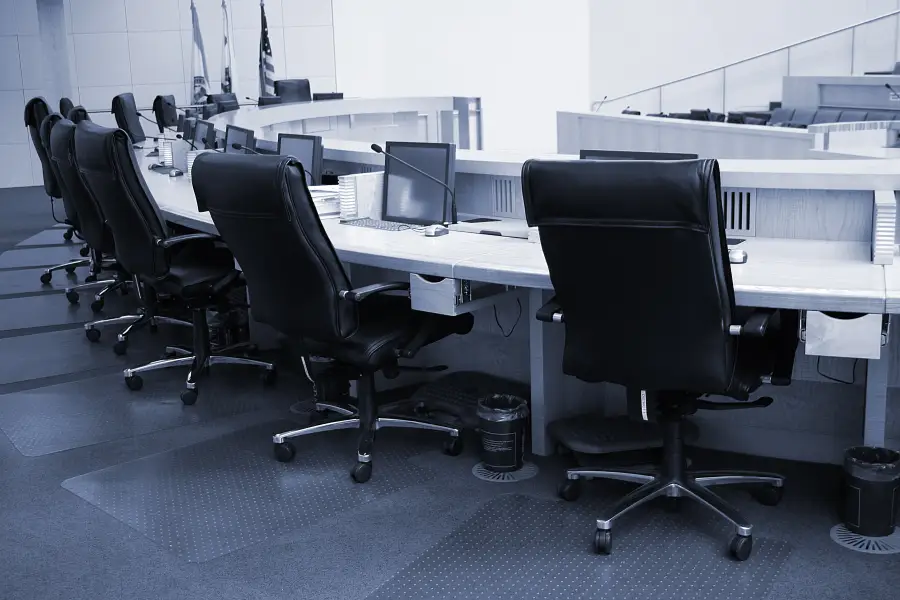 Empty local government council chamber with a curved dais, leather chairs, monitors and microphones.