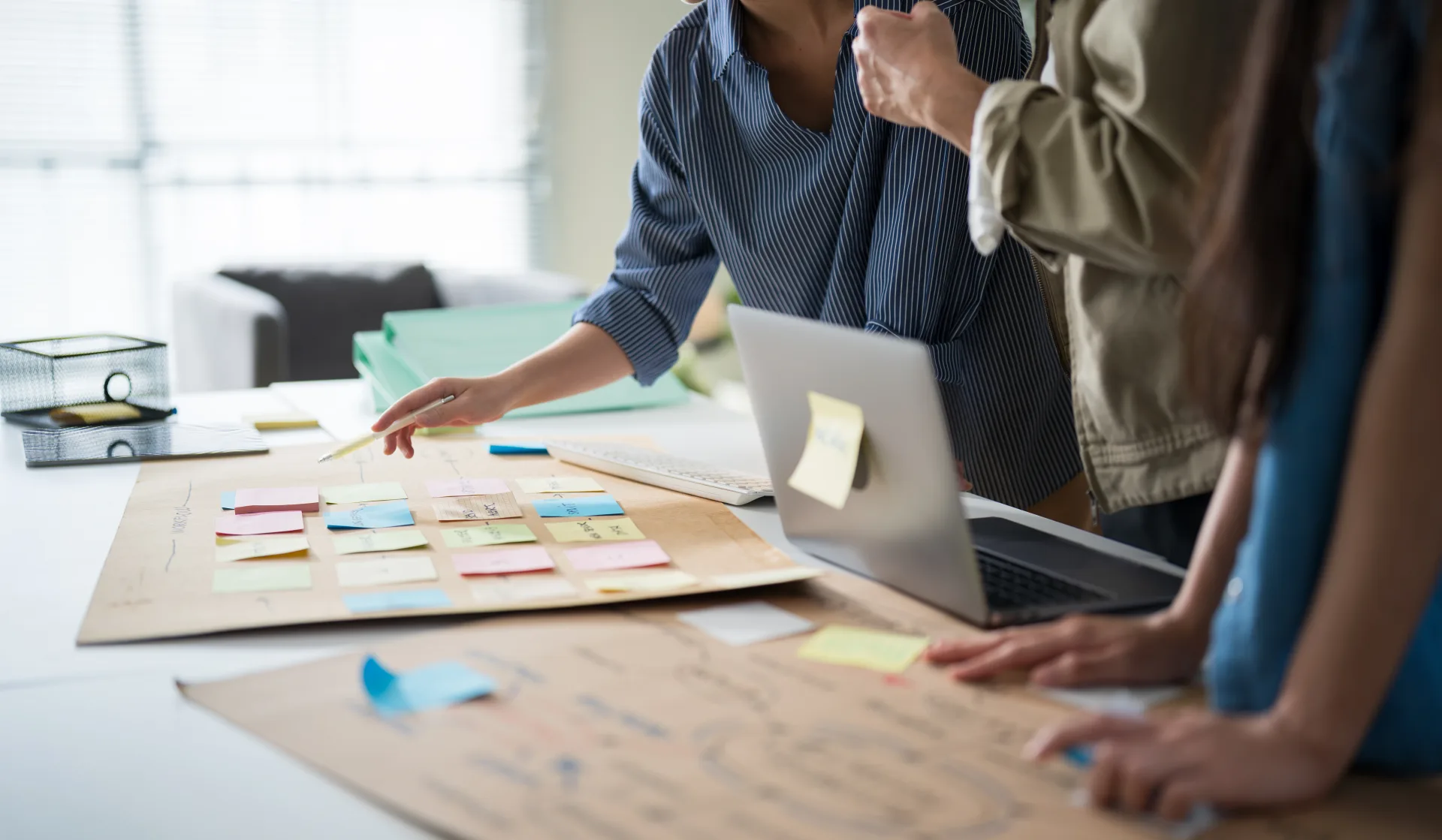 Team members review a large process map covered in colorful sticky notes on a conference table beside a laptop.