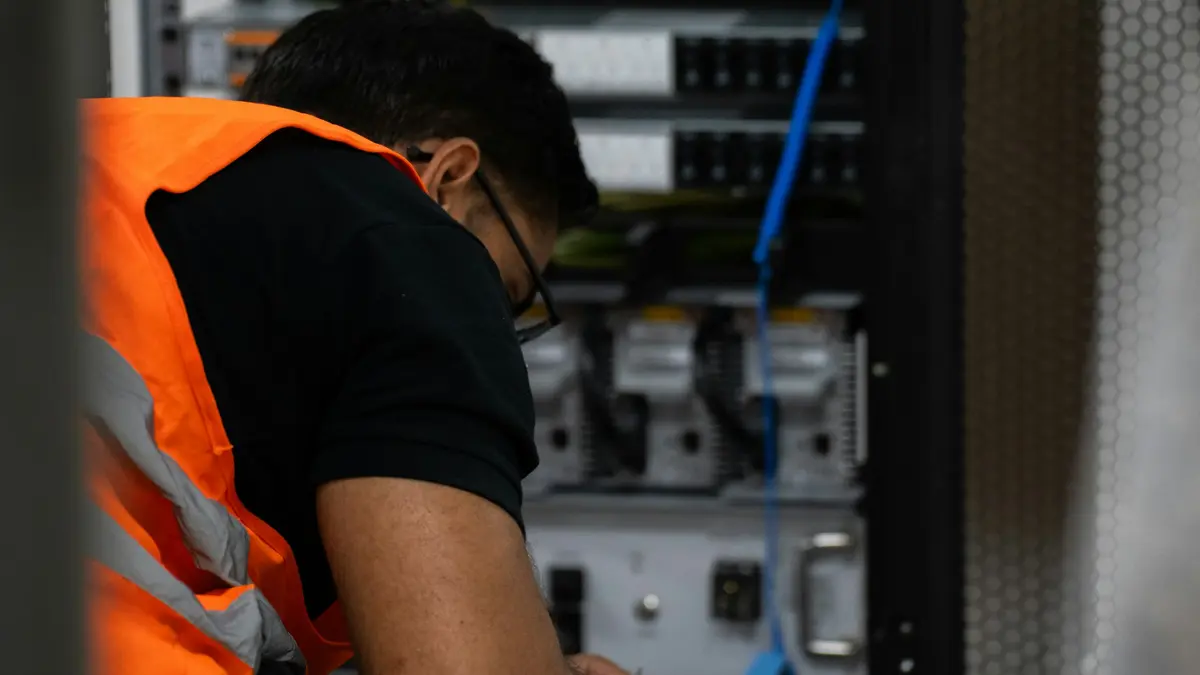 A technician in a high visibility vest working on equipment inside an open server rack.