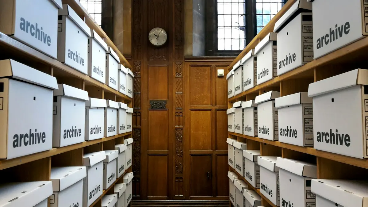 Rows of white storage boxes marked archive, shelved on either side of a wooden door.