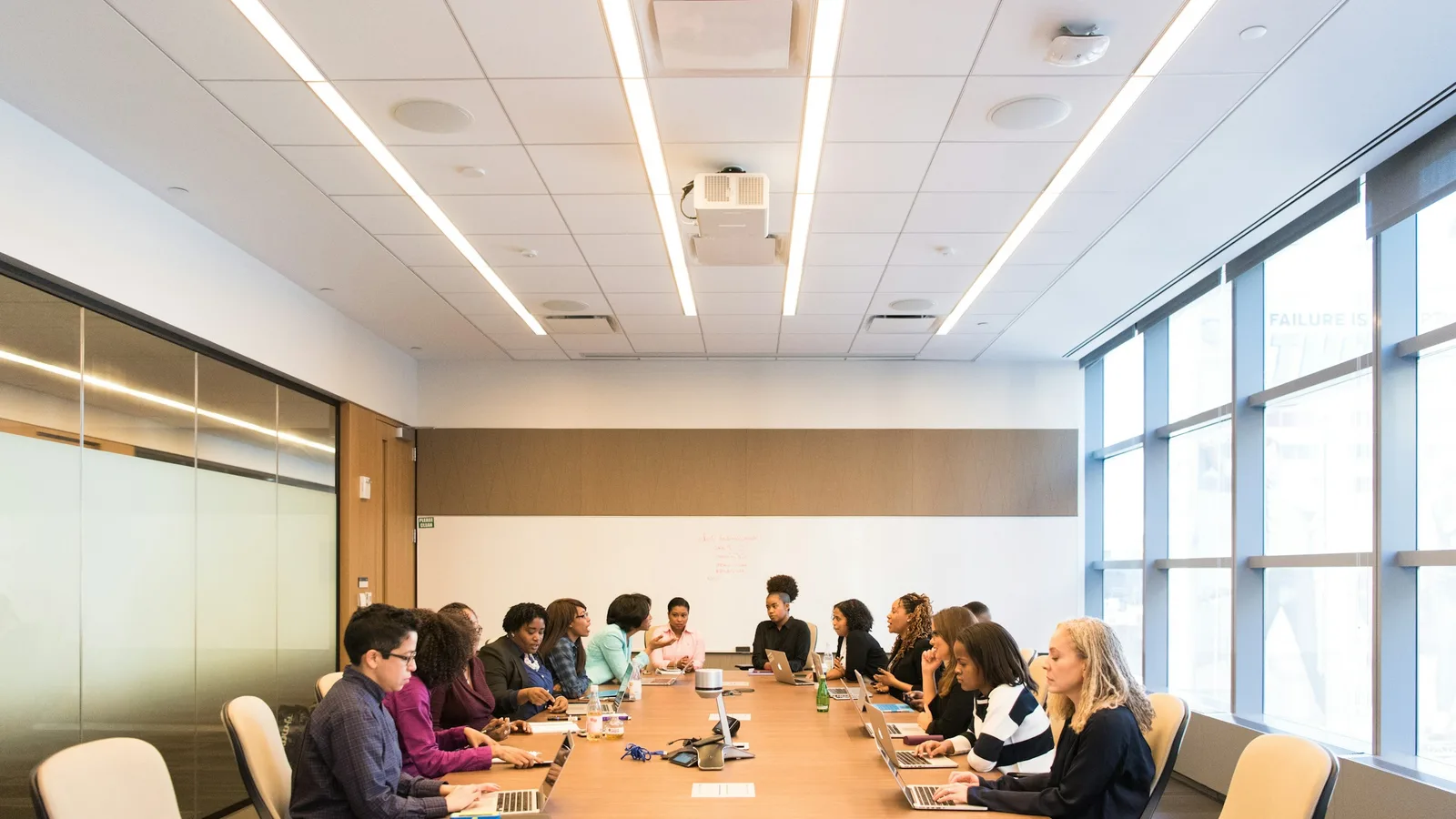 People meeting around a long boardroom table with laptops and papers.