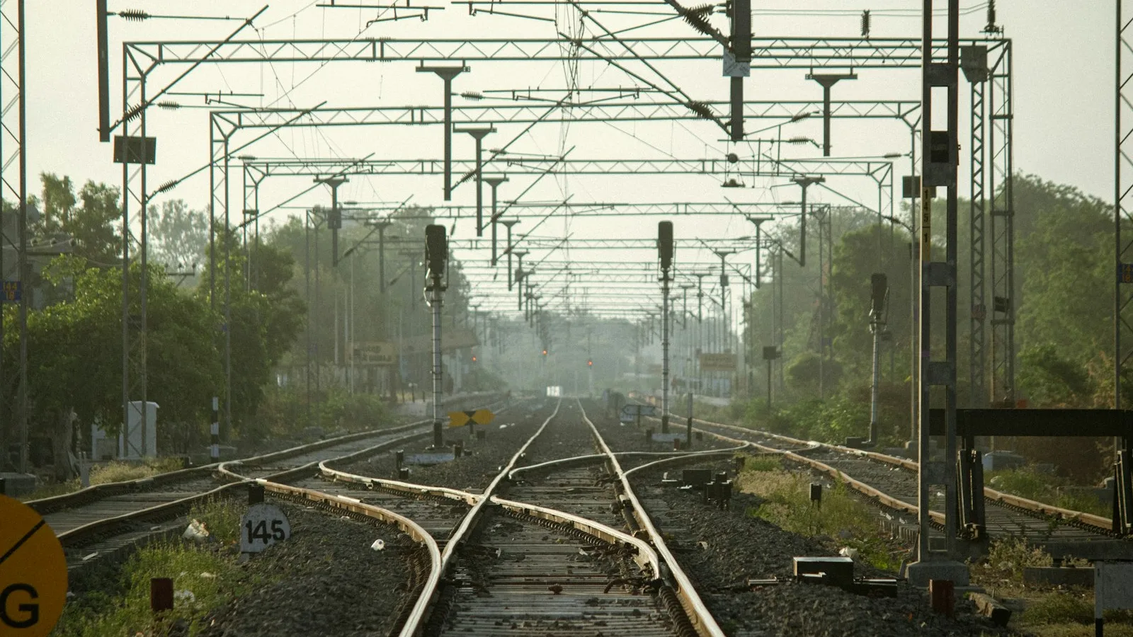 Railway tracks converging beneath overhead lines and signal gantries.