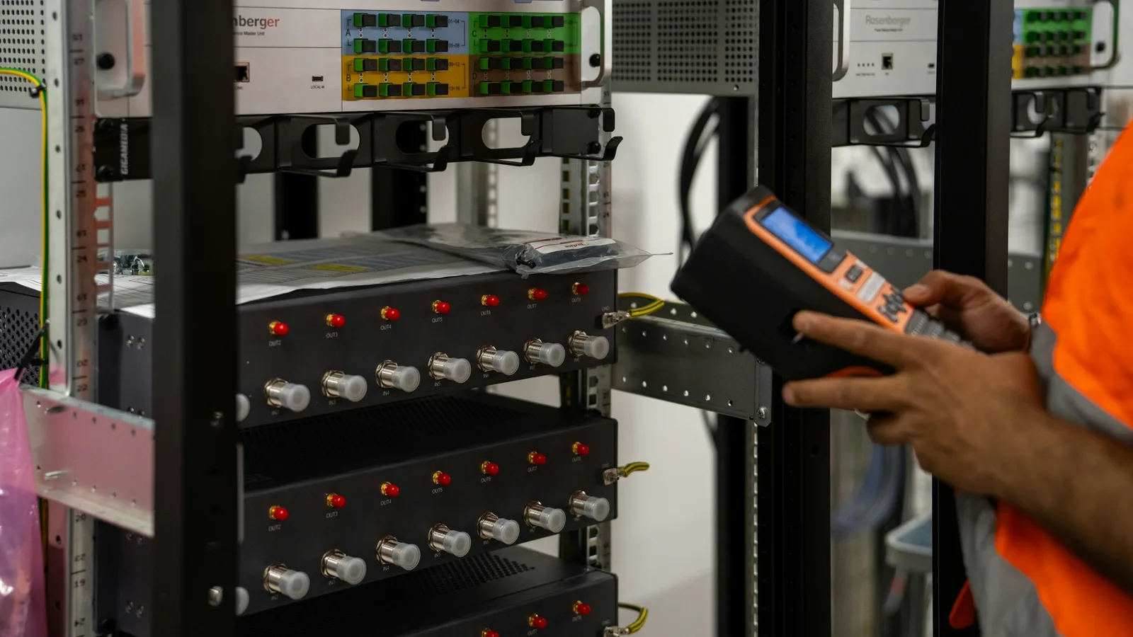 A technician inspecting network equipment racks with a handheld diagnostic tool.