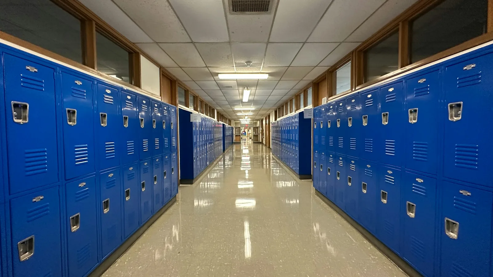 An empty school corridor lined on both sides with blue student lockers.
