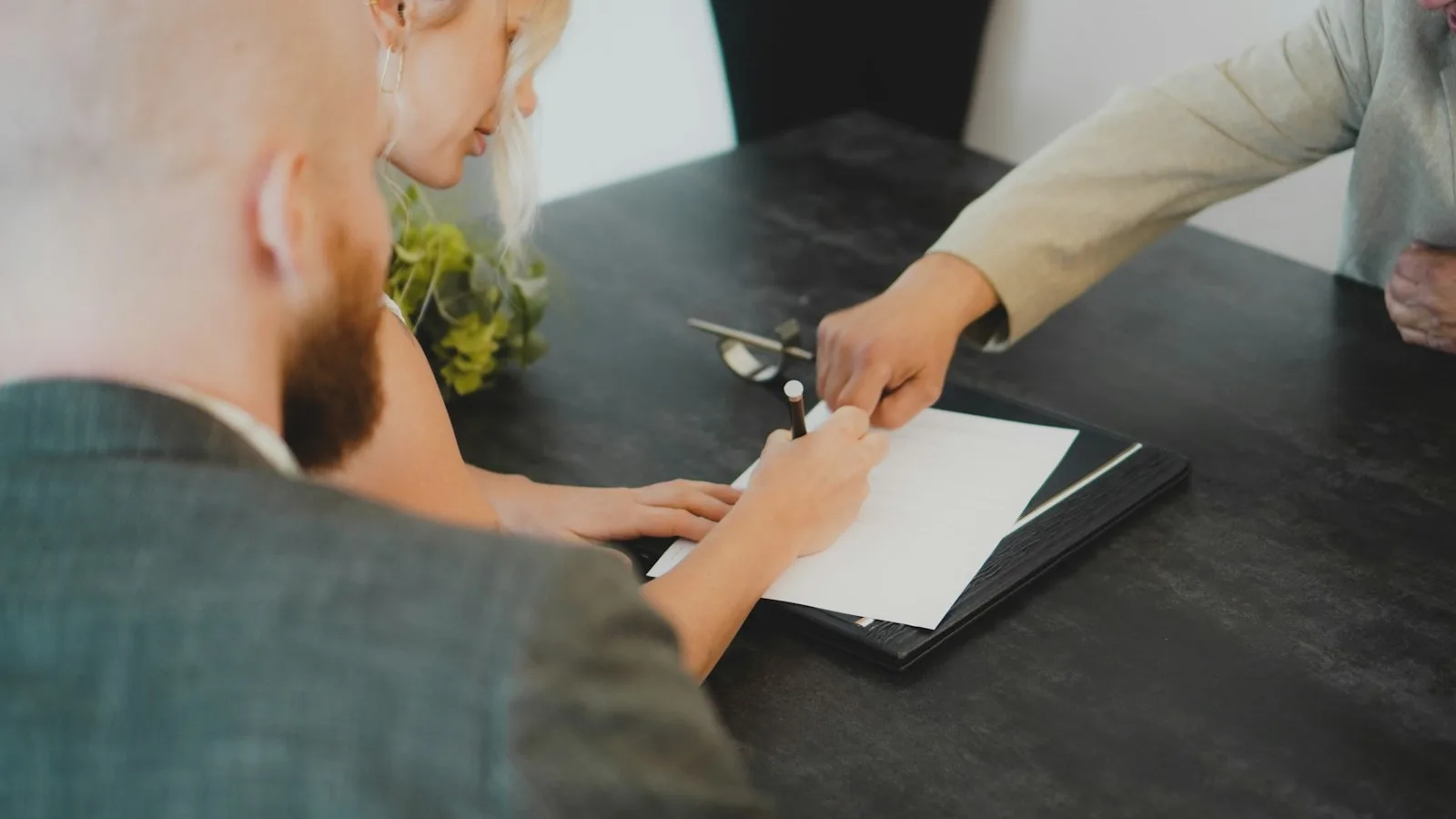A person signing a document on a folder while two colleagues look on across a meeting table.