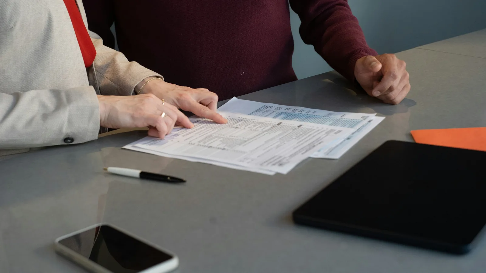 Two colleagues reviewing a printed form together at a desk with a pen.