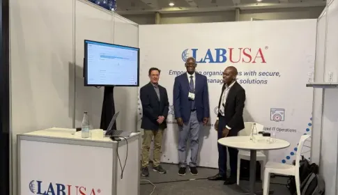 Three LABUSA representatives standing at booth 130 during a trade show; with branded banner and monitor display.