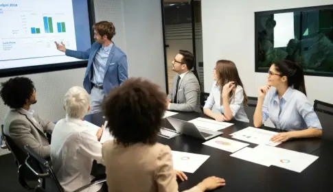 Business professional presents 2018 budget cash flow charts to a diverse team of six colleagues in a modern conference room.