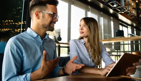 Two business professionals discuss IT solutions in a modern office, one holding a tablet during a collaborative meeting.