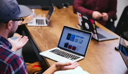 IT professionals collaborate around a wooden table with several laptops open during a team strategy meeting.
