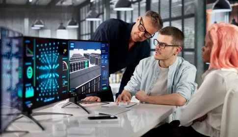 IT professionals collaborate at a workstation reviewing 3D data center and network analytics dashboards on dual monitors.