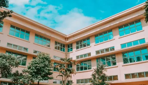 Exterior view of Reyes Hall; a multi-story institutional building with large windows and tropical landscaping under a blue...
