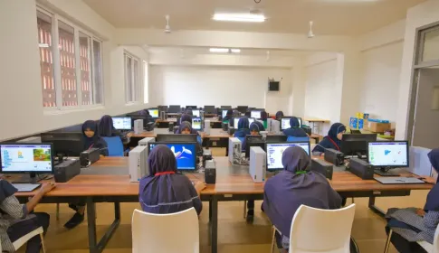Female students in hijabs working on desktop computers in a school computer lab; using Scratch programming software.