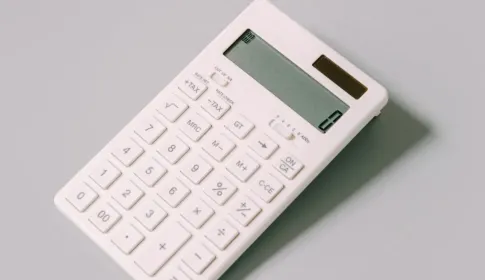 A plain white desk calculator lying on a light gray surface.