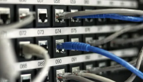 A network patch panel of numbered ports with gray and blue cables plugged into it.