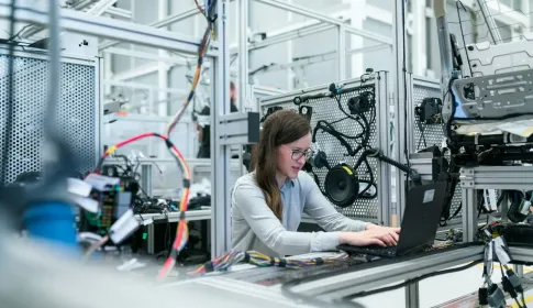 An engineer at a laptop beside an automated production line, monitoring the machinery.