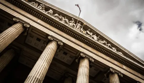 The stone columns and carved pediment of a classical civic building seen from below.