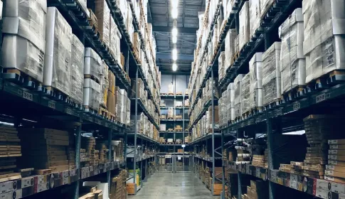 A long aisle between tall warehouse racks stacked with boxed and palletised stock.