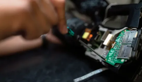 Hands using a small precision tool to examine the exposed circuit boards inside a device.
