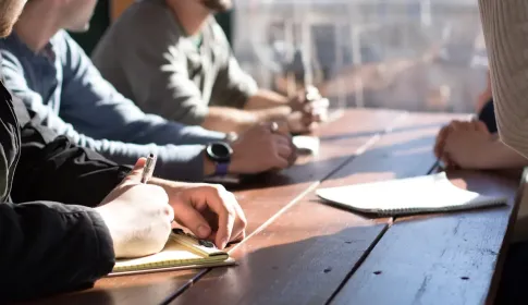 Four colleagues seated along a wooden table, writing notes during a working session.