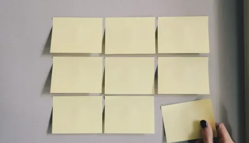 A hand placing a paper note into an ordered grid of notes on a wall.