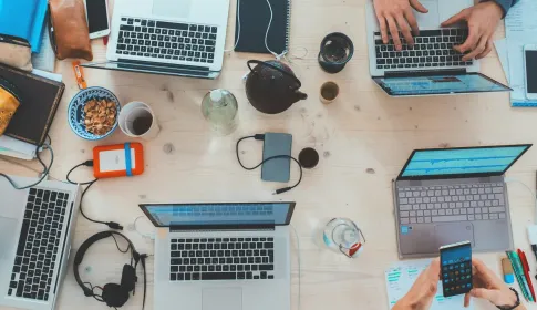 Overhead view of a team working across laptops, tablets and a phone on one shared desk.