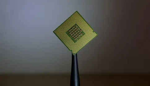 A small gold and green processor die balanced on a black stand against a plain background.