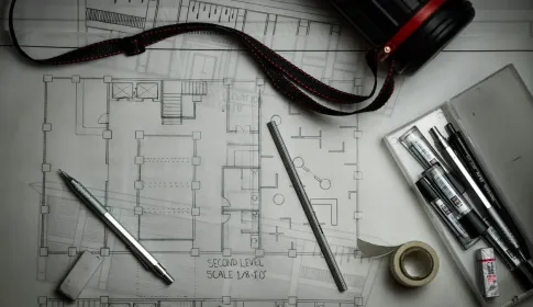 Rolled architectural floor plans on a desk beside a pen, a scale rule and drafting tools.